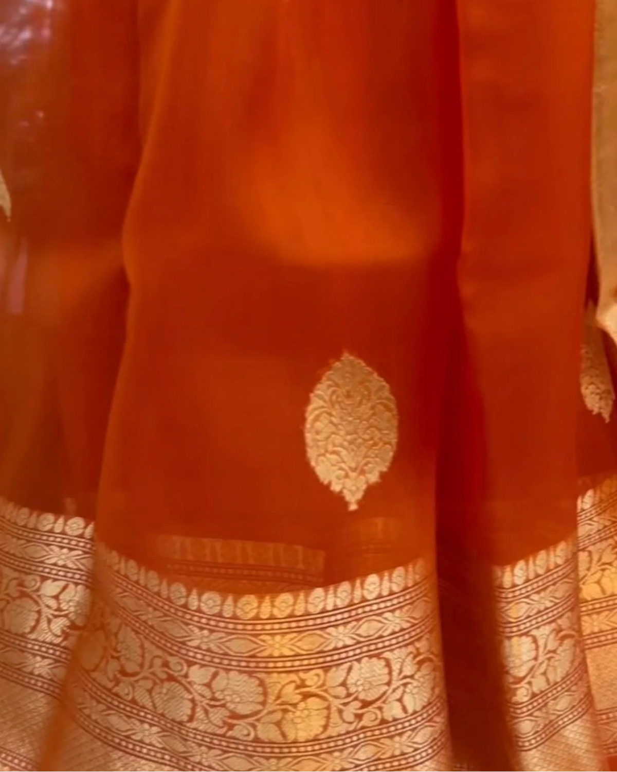 close-up of an orange silk saree with gold zari brocade motifs and a decorative gold border.