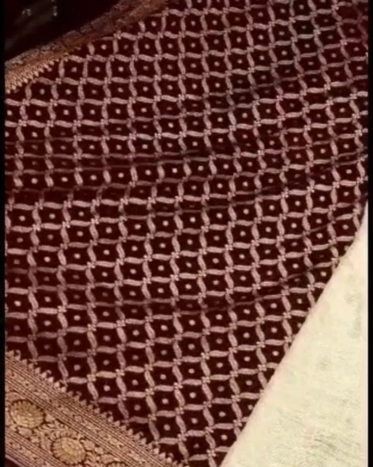 a close-up of a dark brown woven textile with an allover geometric lattice pattern and a decorative border, laid over a light beige textured surface.