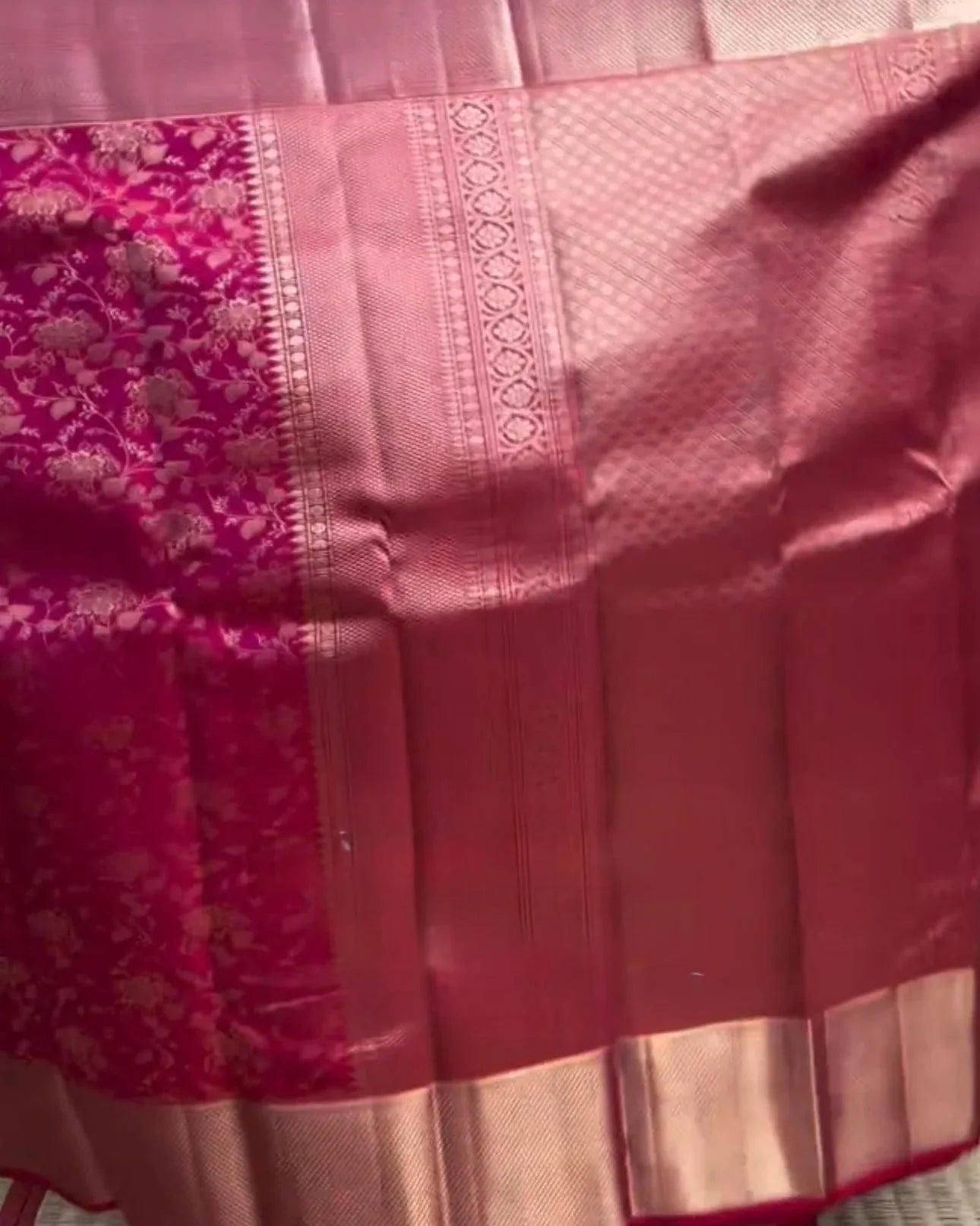 Person holding a pink saree with a patterned border in a store setting.