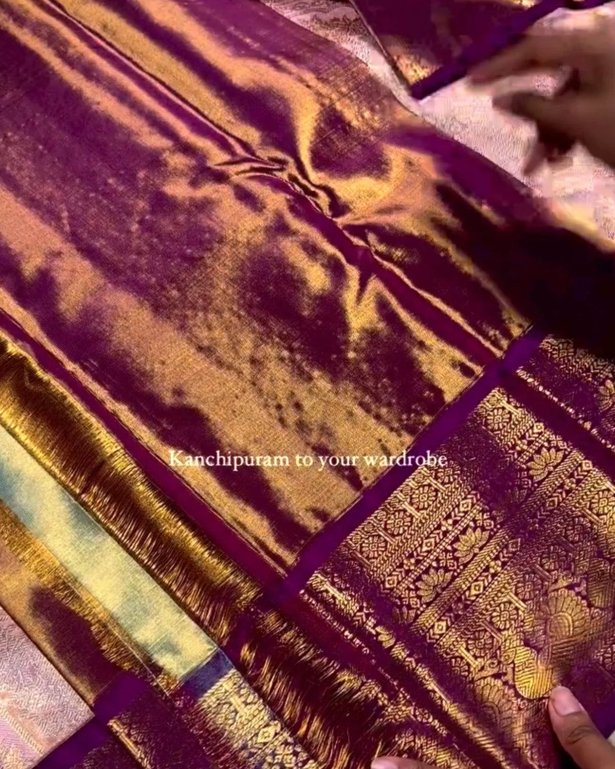 A close-up of a purple and gold zari silk saree with intricate metallic patterns, held by hands to show its texture and drape.