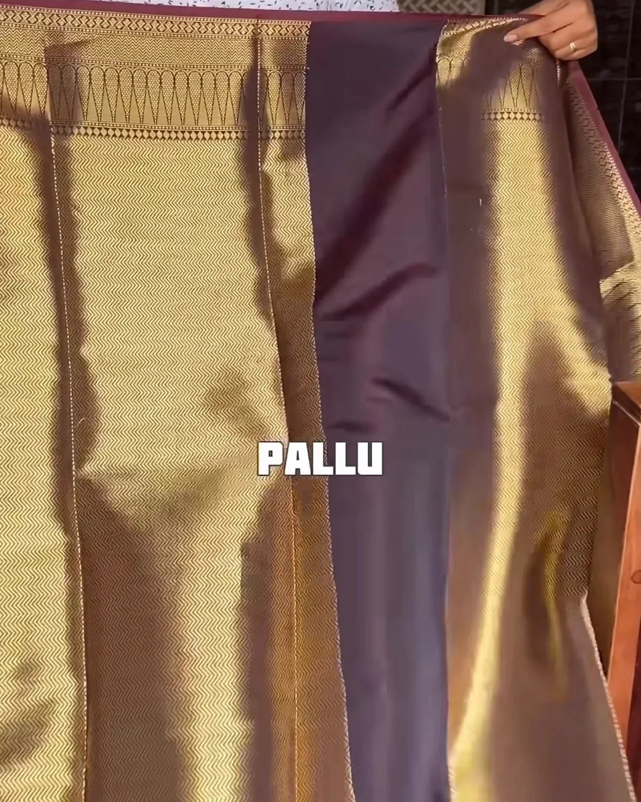 a close-up of a traditional indian pallu section of a saree, showing a wide gold body with a contrasting dark purple border panel held up by a hand. the word 'pallu' is overlaid in white text.