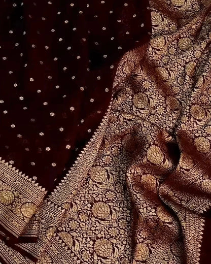 A close-up of a dark maroon or burgundy fabric with dense metallic gold woven floral patterns and small gold dots, likely a textile or scarf.