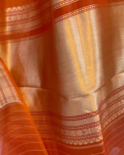 Close-up of an orange and gold woven fabric with metallic zari stripes and ornate border patterns.