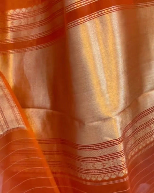 Close-up of an orange and gold woven fabric with metallic zari stripes and ornate border patterns.