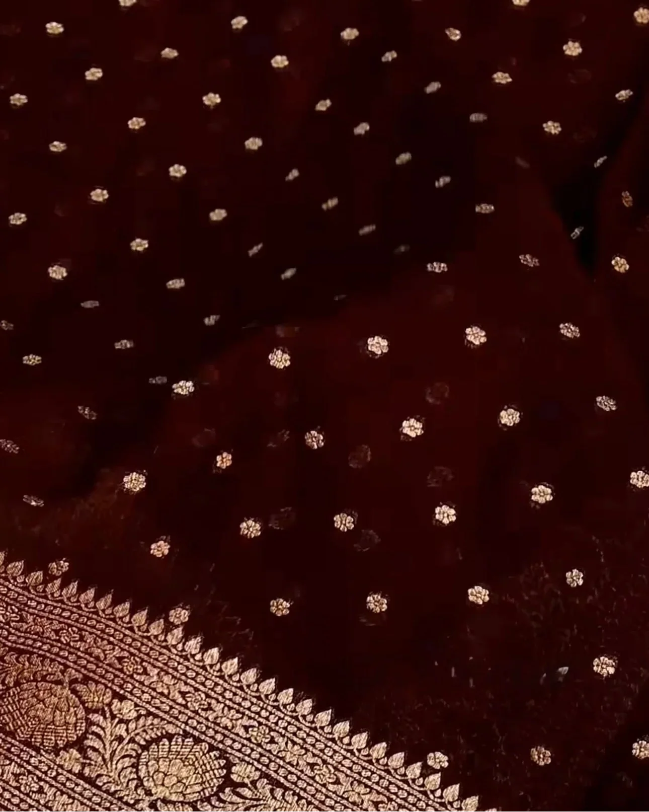 a close-up of a deep maroon or burgundy fabric with small scattered metallic gold floral motifs and a decorative gold border pattern visible along the lower edge.