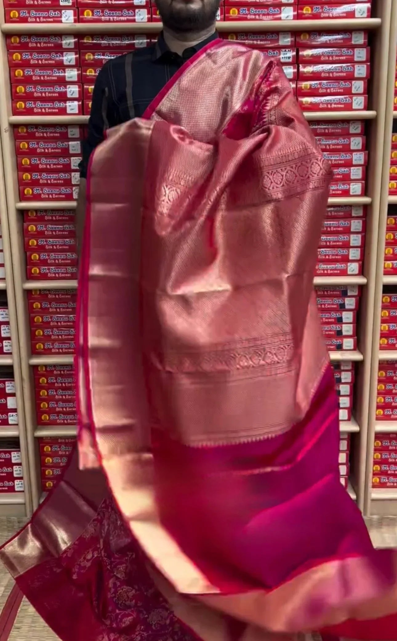 person wearing a pink saree with a blurred background of shelves with products.