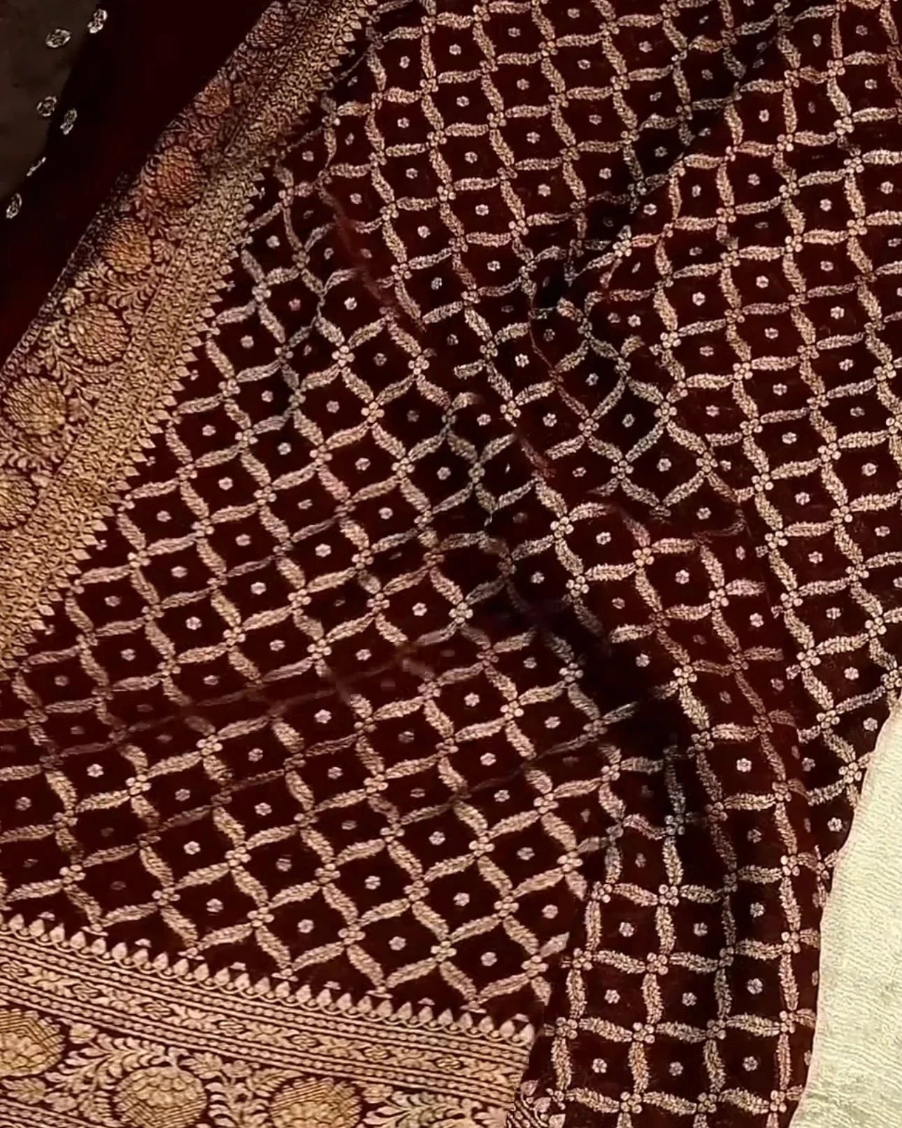 A close-up of a dark brown brocade fabric with an intricate gold geometric lattice pattern and a heavily embroidered border.