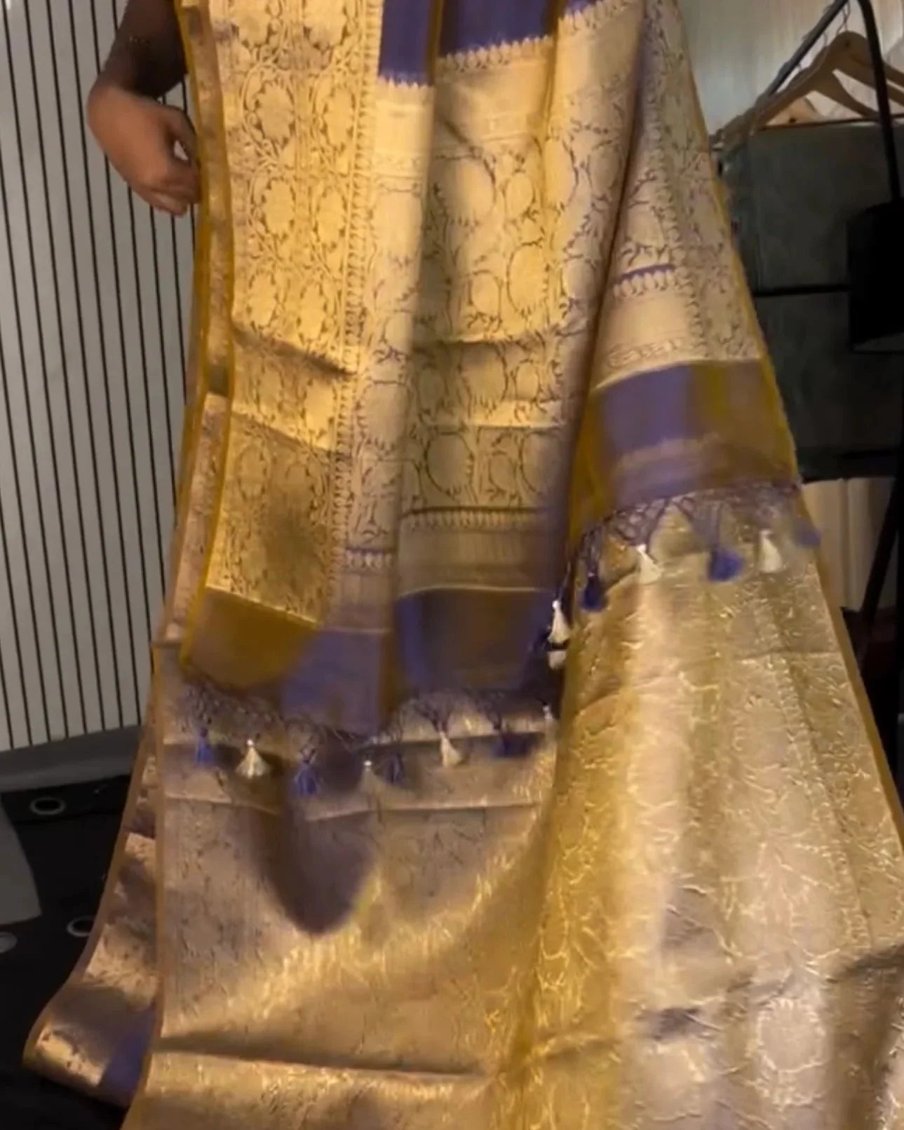 a close-up of a gold and purple banarasi silk saree with intricate zari embroidery and a wide border, draped on a person.