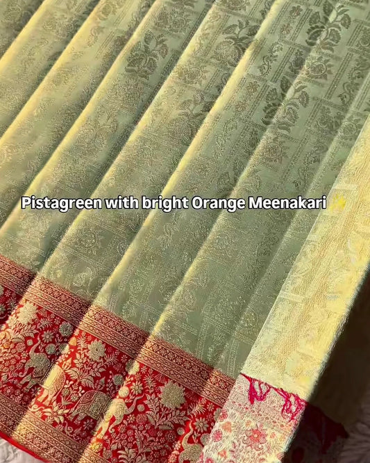 A close-up of a traditional Indian saree fabric, showing the main body in a light pistachio green with a golden floral brocade pattern, and a wide border in red and gold with floral motifs. Text overlay reads 'Pistachio green with bright Orange Meenakari'.