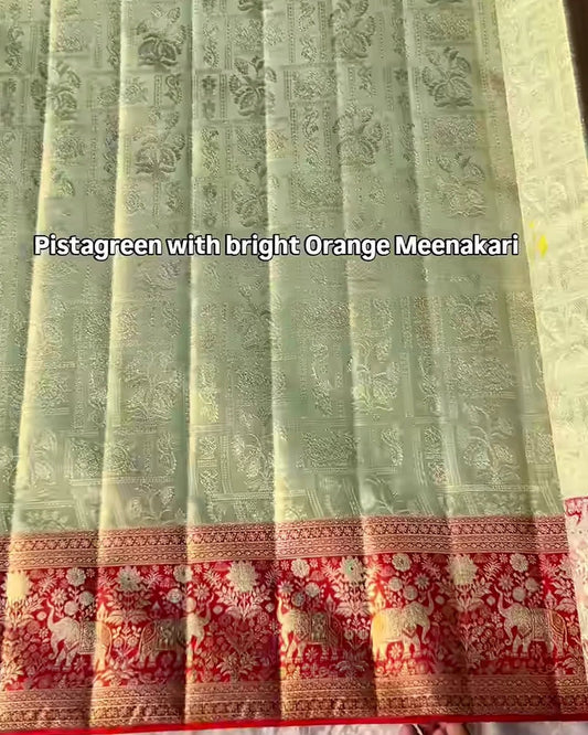 A folded and pleated light pistachio green Banarasi silk saree with intricate gold zari floral motifs, featuring a prominent orange and red floral border.