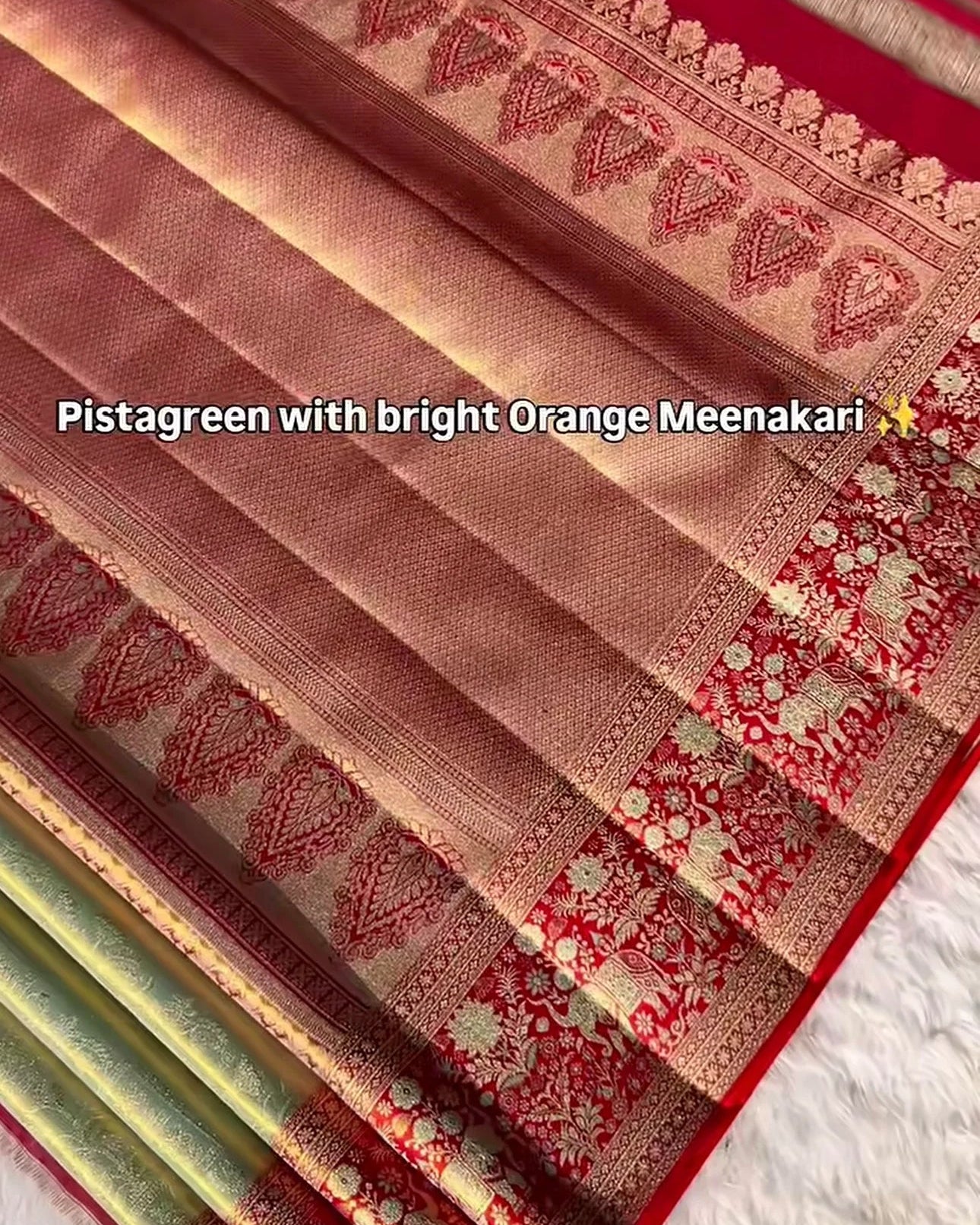 a close-up of a folded saree fabric in pistachreen with bright orange meenakari work, showing the woven border patterns and red border, with a text overlay describing the color combination.