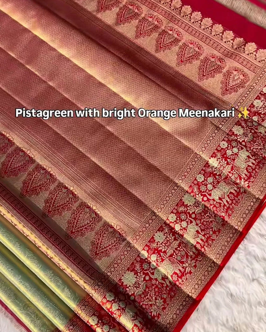 A close-up of a folded saree fabric in pistachreen with bright orange meenakari work, showing the woven border patterns and red border, with a text overlay describing the color combination.