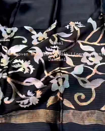 A close-up of a black silk or satin fabric with metallic gold and silver floral brocade patterns and a striped gold border. White text overlay reads 'Jamal Handwoven Mercerized Silk Linen Jacquard Jamdani'.